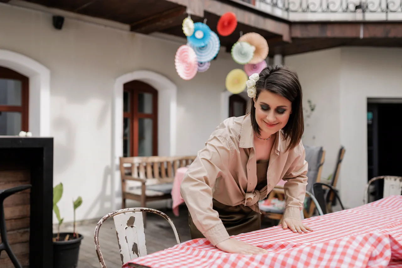 A smiling event planner setting a gingham table in a festive courtyard